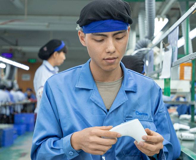 a male worker sitting at the assembly line is assembling an infrared thermometer